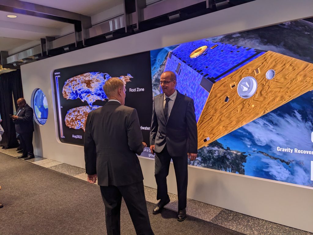 NASA Administrator with farmer Dwane Roth standing in from of a video in which Dwane is featured.